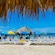 Sunbathers sit in lounge chairs underneath umbrellas on a picturesque beach
